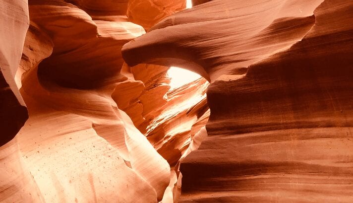 A photo of Antelope Canyon with orange and red rock walls that have been shaped into wave-like forms by years of water erosion, casting beautiful shadows and light.