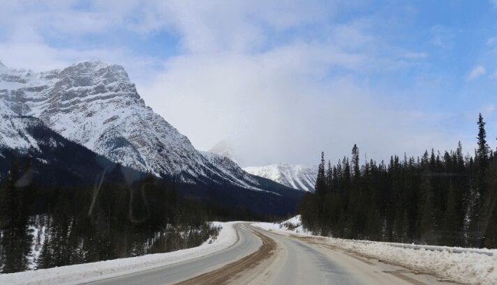 The Icefields Parkway covered in snow, with towering mountains and frozen lakes creating a stunning, winter wonderland scene.