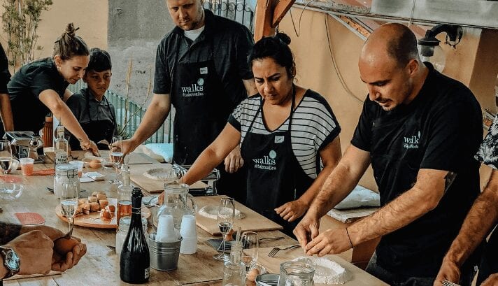 People gathered around a table in Rome, skillfully making fresh, homemade pasta, rolling and shaping the dough into classic Italian varieties.