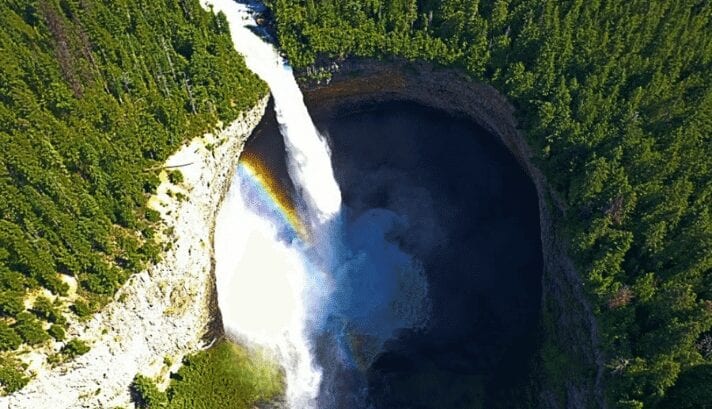 "A waterfall at Wells Gray Provincial Park with a rainbow in the mist, surrounded by green trees.