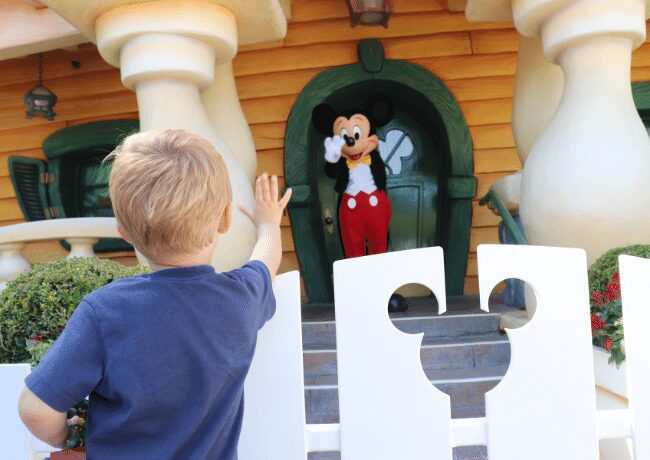 From the back, a young child joyfully waves at Mickey Mouse while immersed in the enchanting world of Disneyland in California. It's a heartwarming sight that encapsulates the pure magic and happiness found within the iconic theme park.