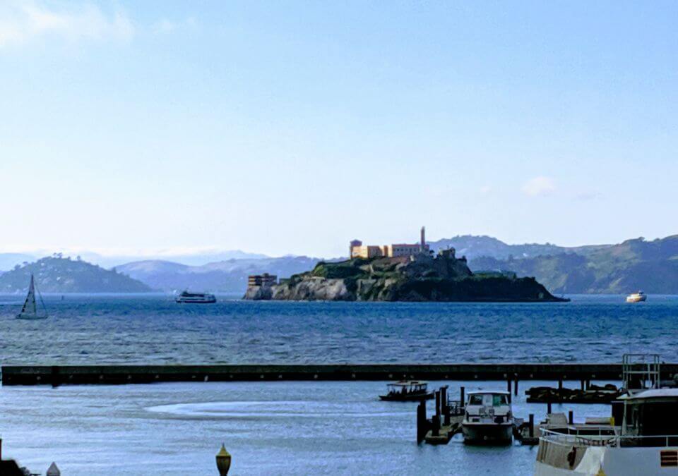 Panoramic view of Alcatraz prison from San Francisco, showcasing the imposing structure on the island amidst the picturesque backdrop of the city skyline and the shimmering waters of the bay.